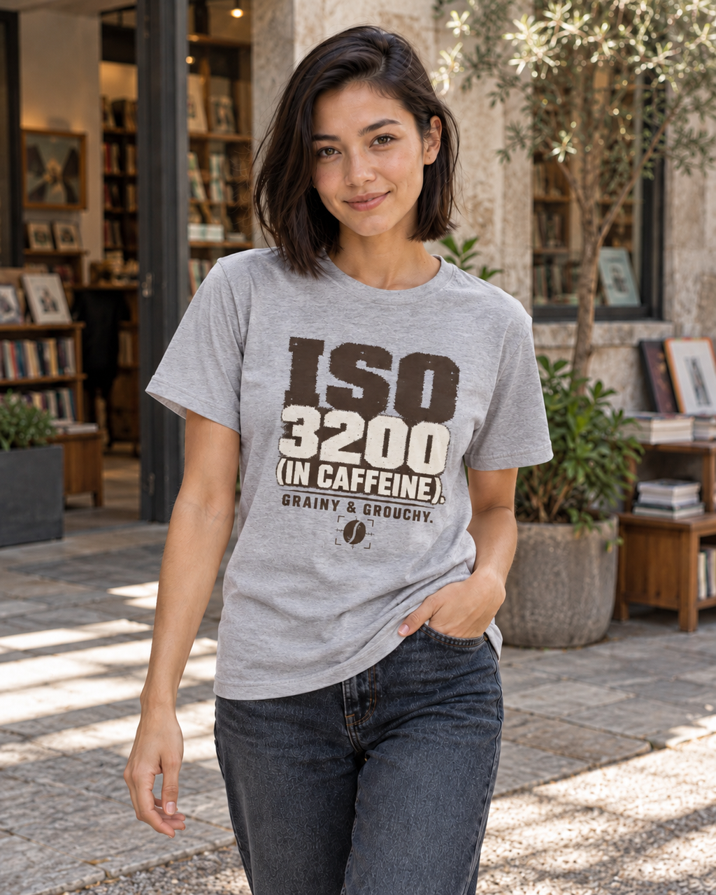 A woman wearing a light sport gray graphic t-shirt with bold black and white text reading 'ISO 3200 (IN CAFFEINE). GRAINY & GRECHY.